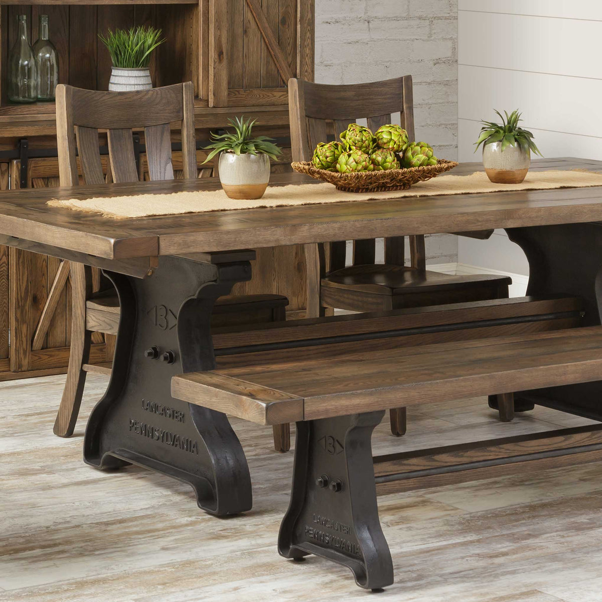 Slat back dining chairs in a driftwood finish at a plank table with black cast iron trestle bases and matching bench