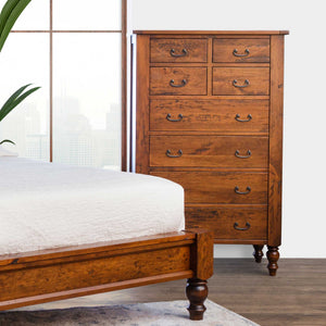Tall cherry chest of eight drawers with antique bronze bail pulls and turned feet beside a bed footboard