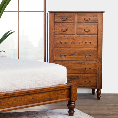Tall cherry chest of eight drawers with antique bronze bail pulls and turned feet beside a bed footboard