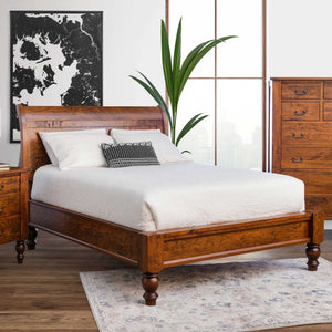 Cherry sleigh bed with low footboard and turned feet styled with white bedding, nightstand and tall chest