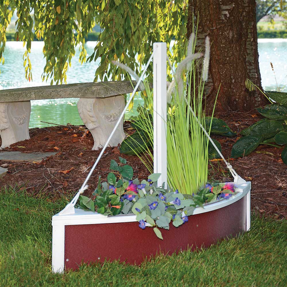 Red and white sailboat shaped poly planter filled with grasses and purple flowers under a tree