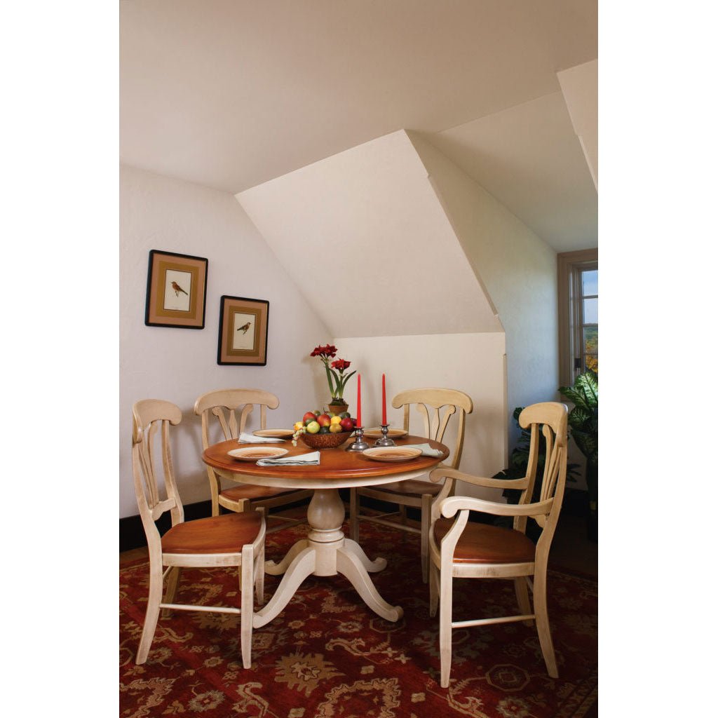 Round single pedestal dining table with cherry top and cream painted base surrounded by four painted chairs in an attic dining nook