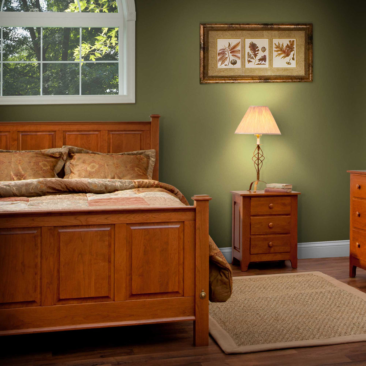 Cherry raised panel footboard in a green bedroom with a three drawer nightstand and lamp