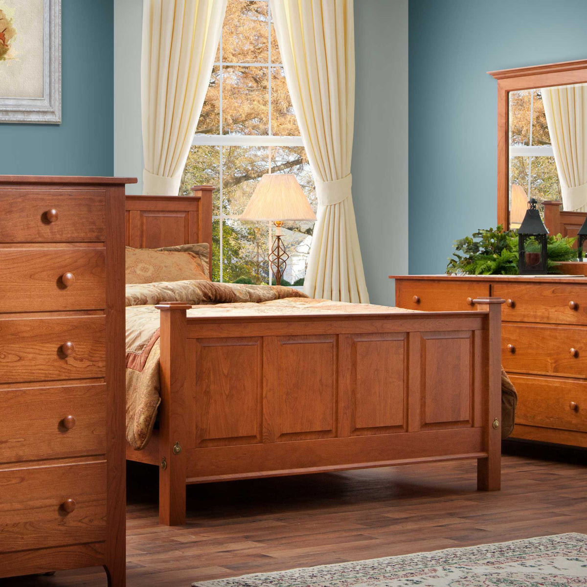 Cherry panel bed footboard flanked by a tall chest and dresser with mirror in a blue bedroom