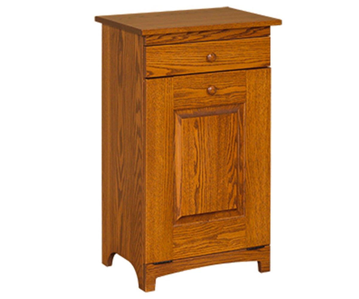 Oak trash bin cabinet with a top drawer above a tilt-out paneled door with wood knobs, on a white background