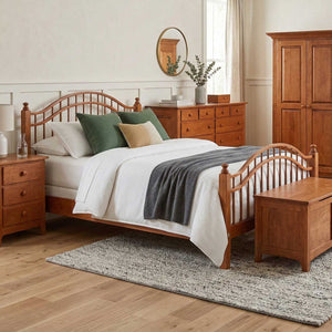 A wooden bed frame with a curved spindle headboard and footboard, styled in a warm, neutral-toned bedroom with matching wooden furniture, including a nightstand, dresser, wardrobe, and bench, on a gray rug.