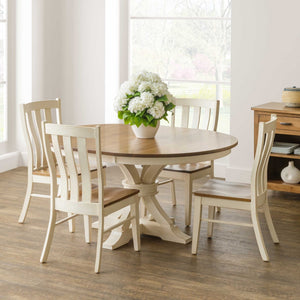Round expandable pedestal dining set with an antique white base, oak top and four slat back chairs in a sunlit dining room