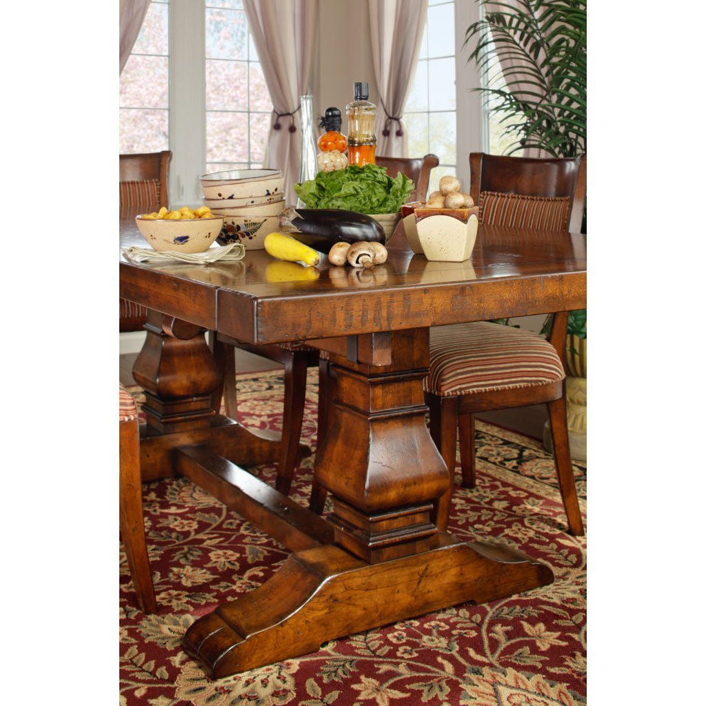 Close view of a rustic brown pedestal dining table topped with fresh vegetables and pottery, flanked by striped upholstered chairs
