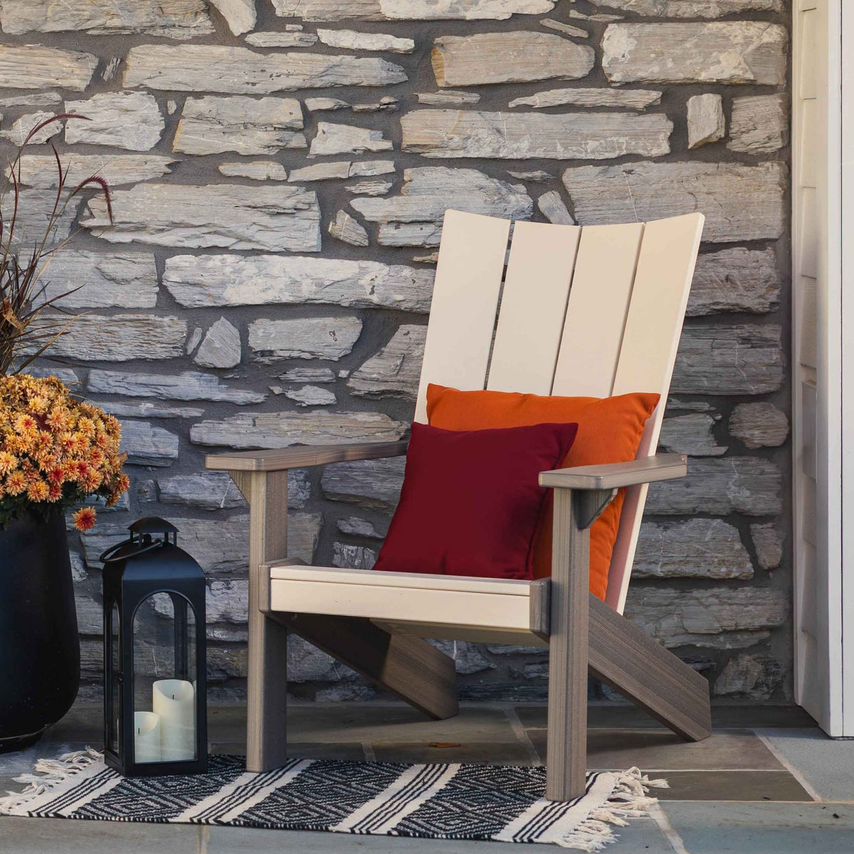 Two-tone cream and gray modern Adirondack chair on flagstone with a lantern, mums and striped rug