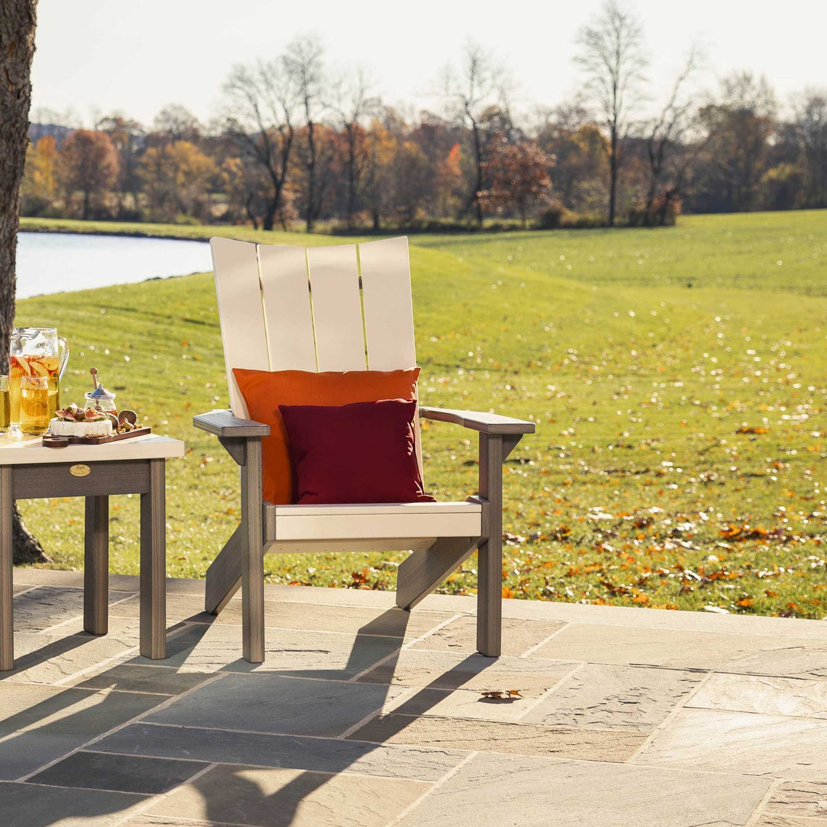 Angled view of a cream and taupe modern Adirondack chair with a four-slat back beside a matching side table