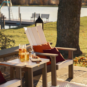 Cream modern Adirondack chair beside a square side table set with iced tea and cheese overlooking a lake