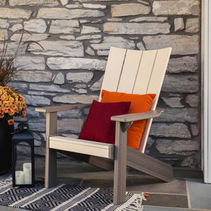 Cream and driftwood modern Adirondack chair with orange and red pillows on flagstone by a stone facade