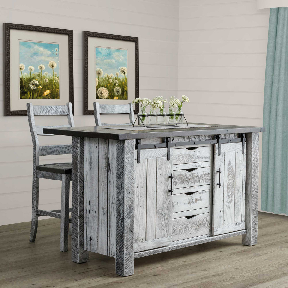 Kitchen island in distressed gray barnwood with a charcoal top, sliding doors and drawers, styled with two stools and flowers