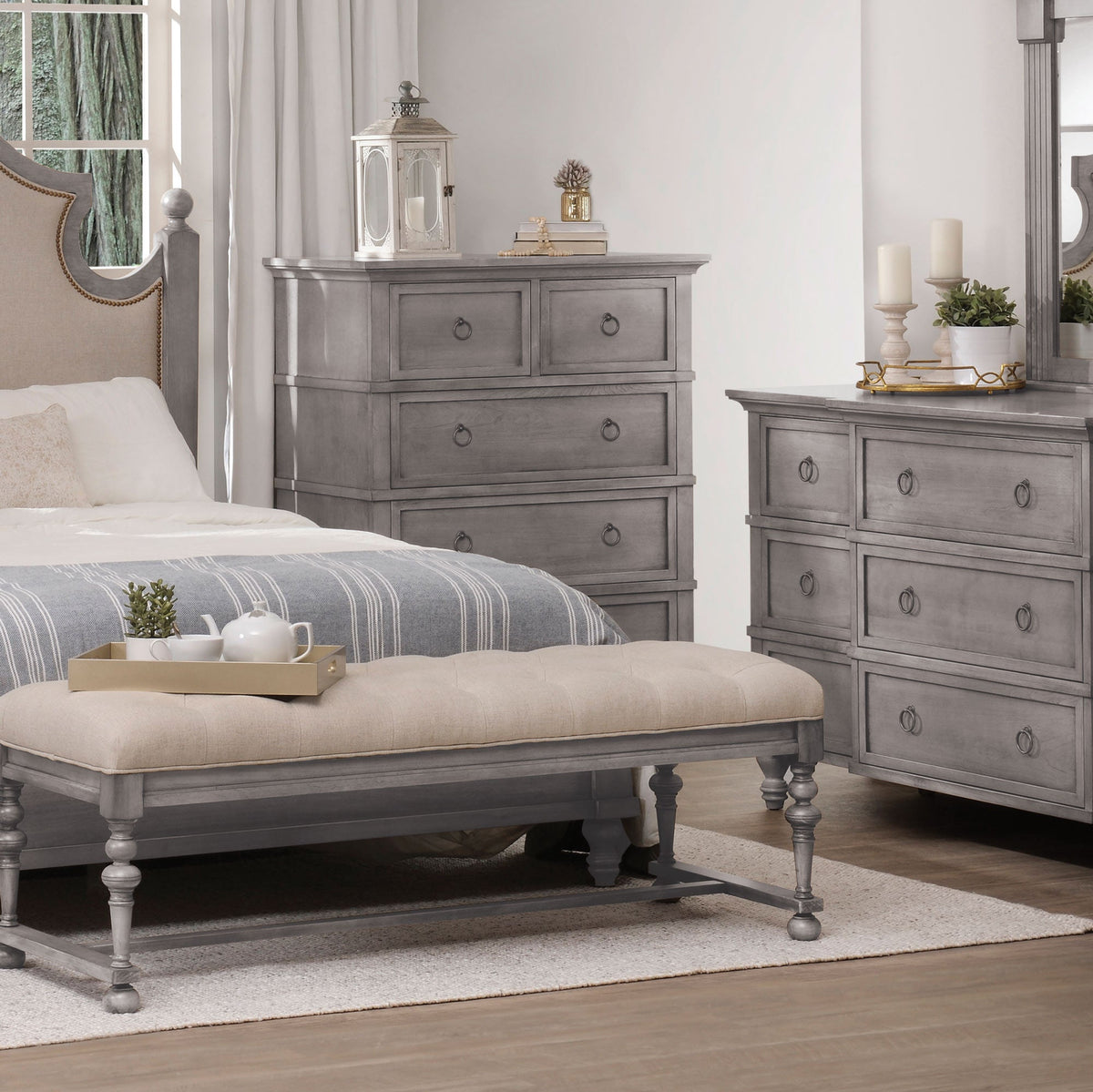 Gray five-drawer chest and dresser beside a linen tufted bedroom bench with turned legs and a tea tray