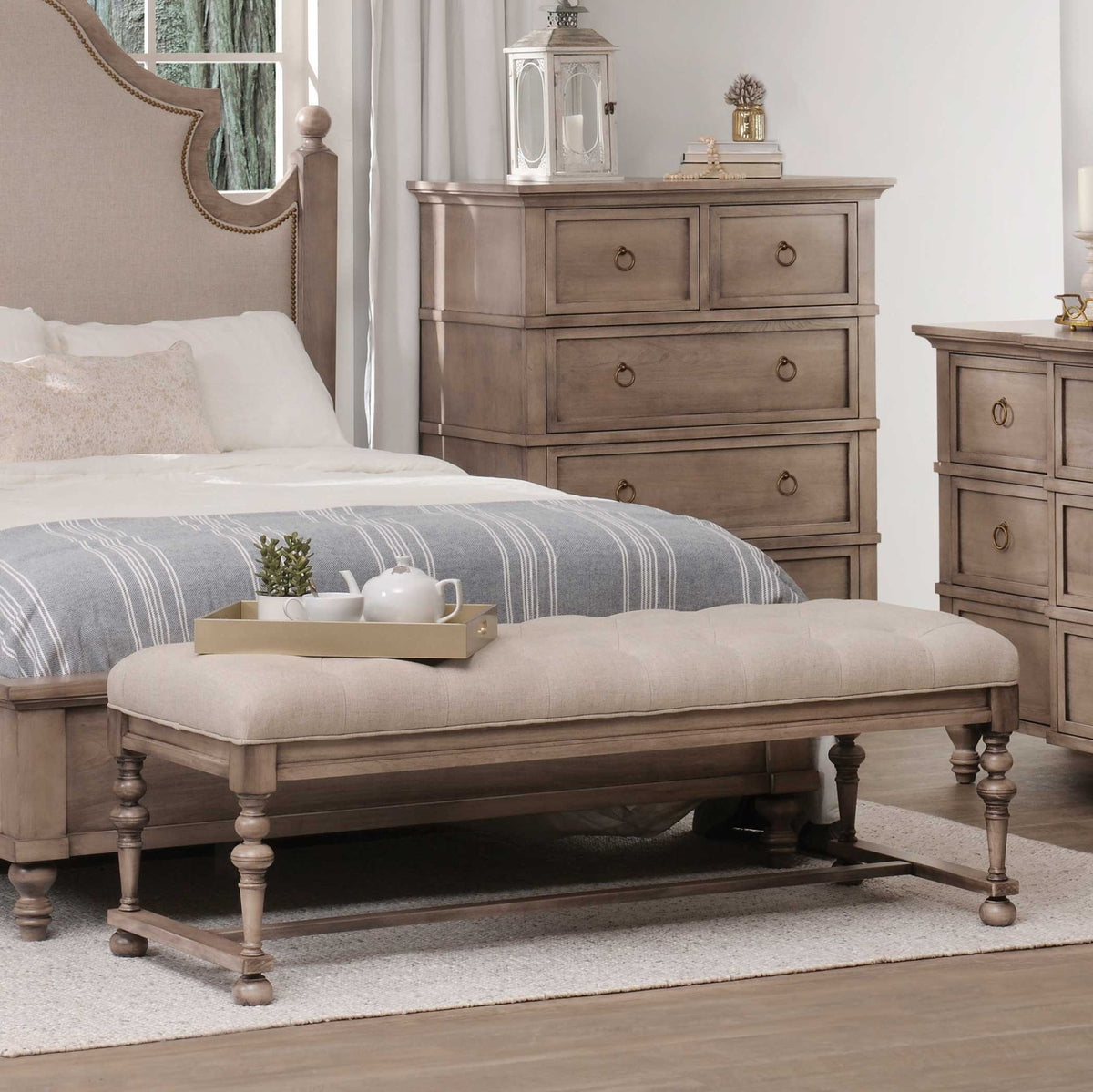 Taupe cushion bench with tufted linen seat and turned legs styled at the end of a bed with a tea tray