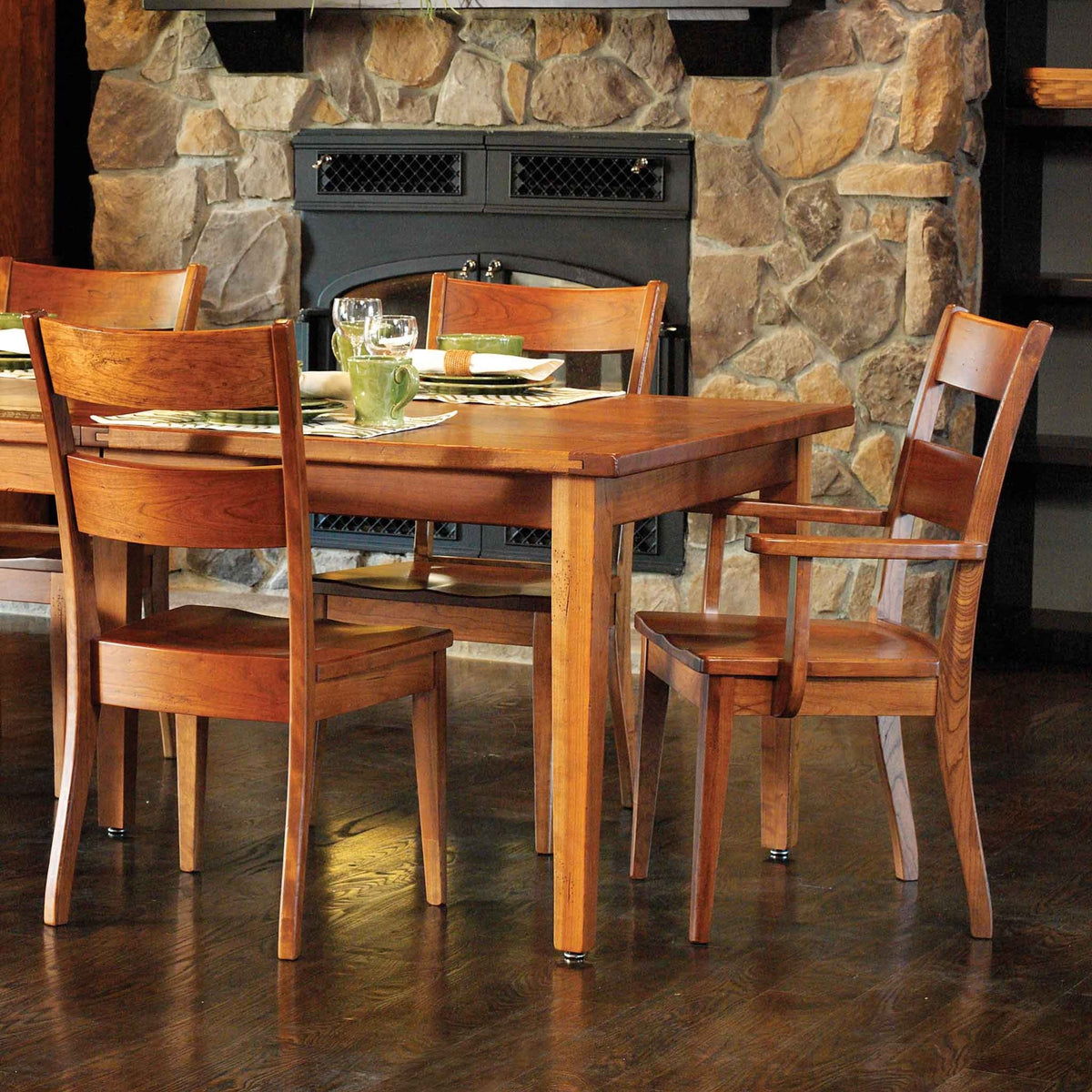 Cherry dining table with saddle-seat side and arm chairs set for dinner in front of a stone fireplace