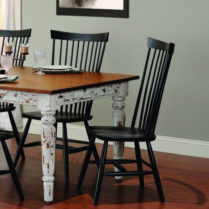 Black windsor dining chairs with turned legs around a distressed white farmhouse table set for a meal