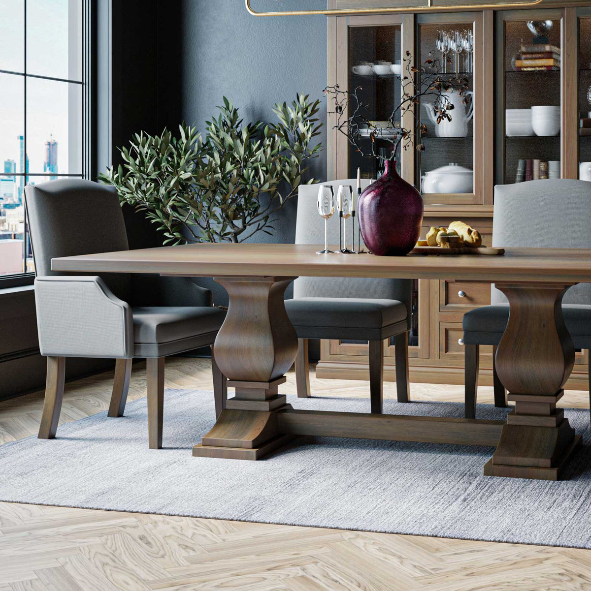 Gray upholstered dining chairs around a light oak double pedestal table with a china cabinet behind