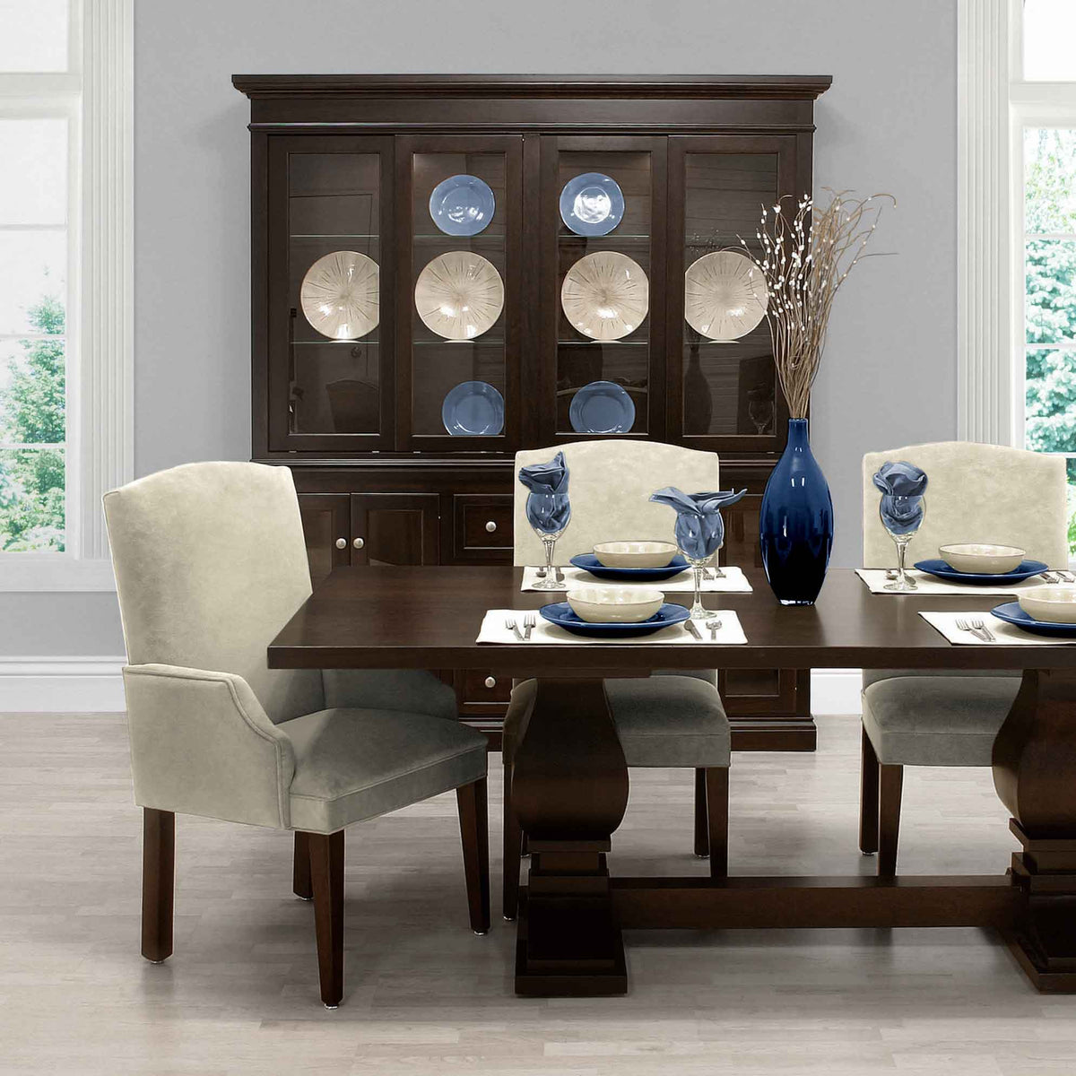 Dark espresso china cabinet with lighted glass doors displaying plates behind an upholstered dining set
