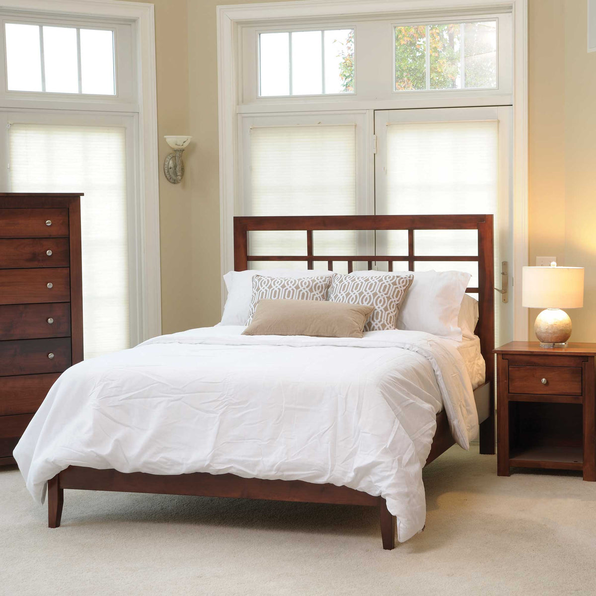 Poughkeepsie lattice bed in cherry dressed in white bedding, its open geometric headboard framed by shaded windows