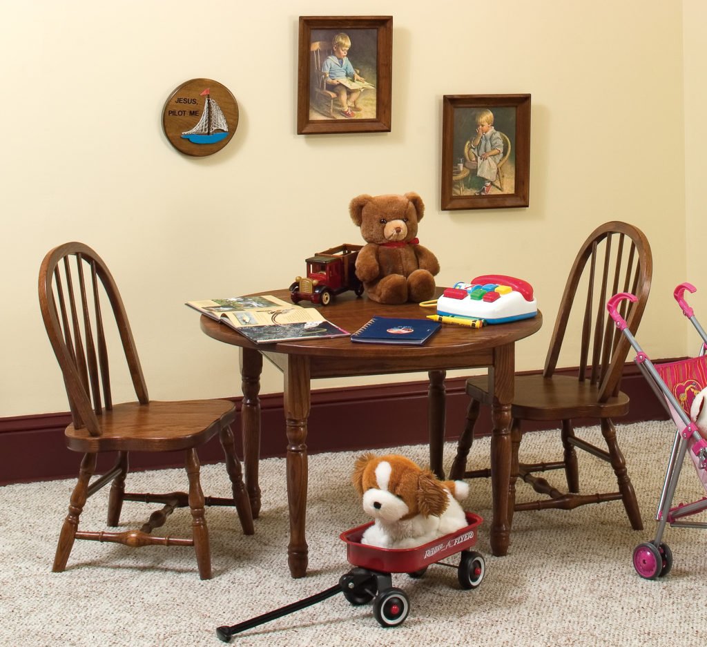 Child sized round table and two arrow back chairs in a dark oak finish, styled with a teddy bear, books and toy wagon