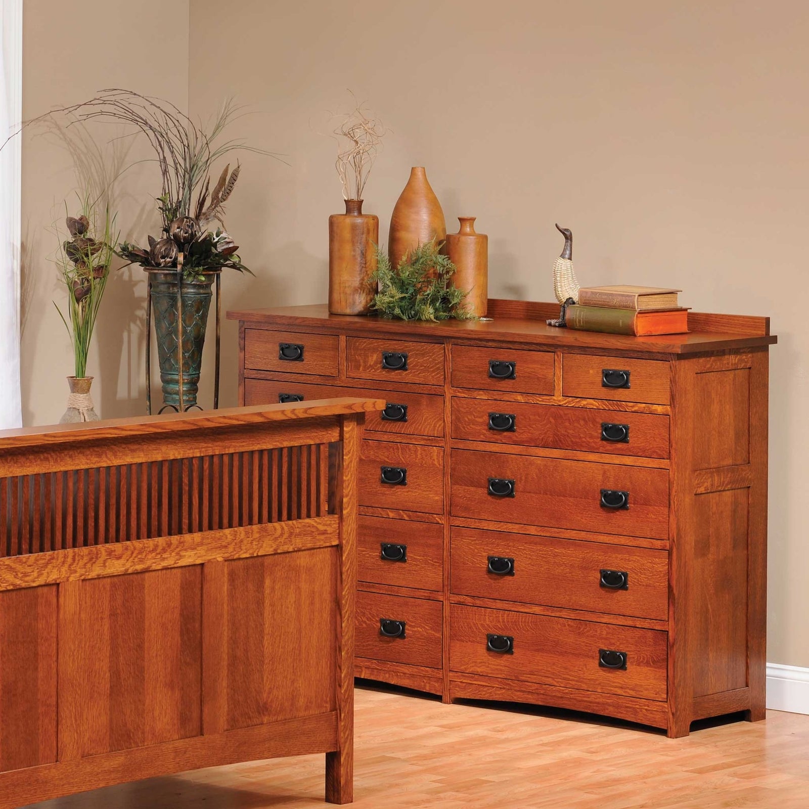 Twelve-drawer Mission oak dresser styled with turned vases and books, standing beside a spindle bed footboard