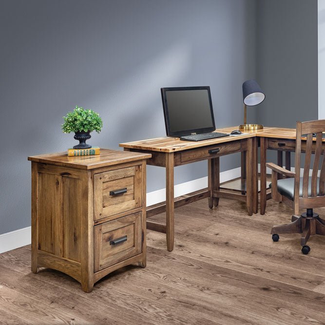 Rustic hickory two drawer file cabinet beside an L shaped writing desk with laptop and lamp in a home office