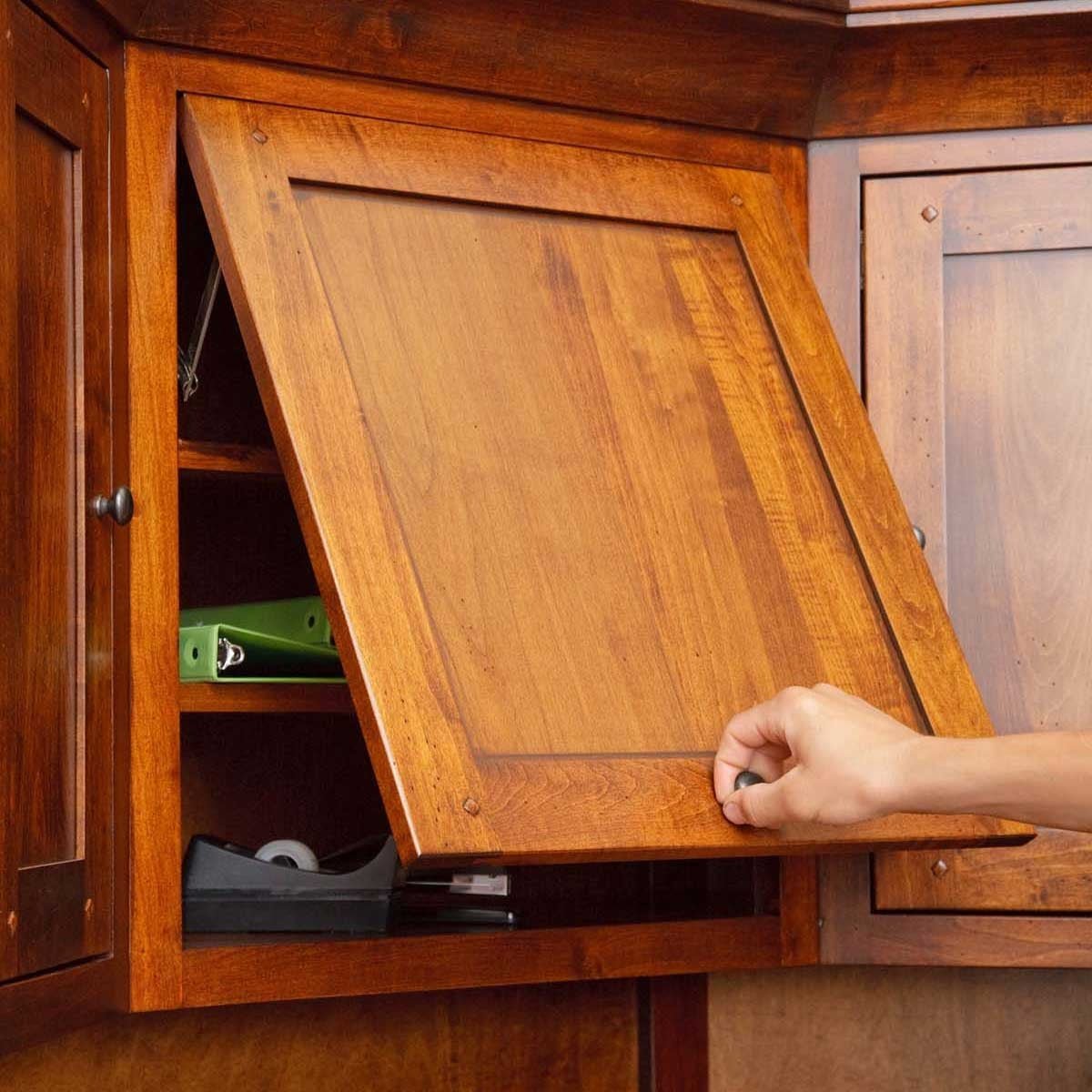 Hand lowering a flip down hutch door on a wood office cabinet, revealing binders and desk supplies inside