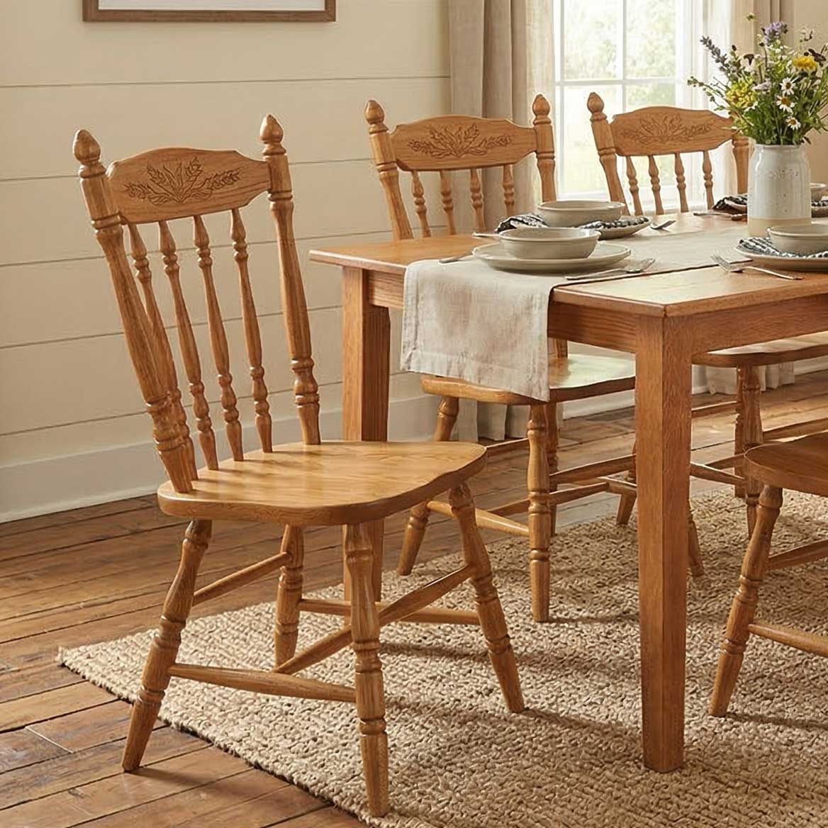Oak Windsor chairs with carved wheat crest and turned spindles around a farmhouse dining table set for a meal