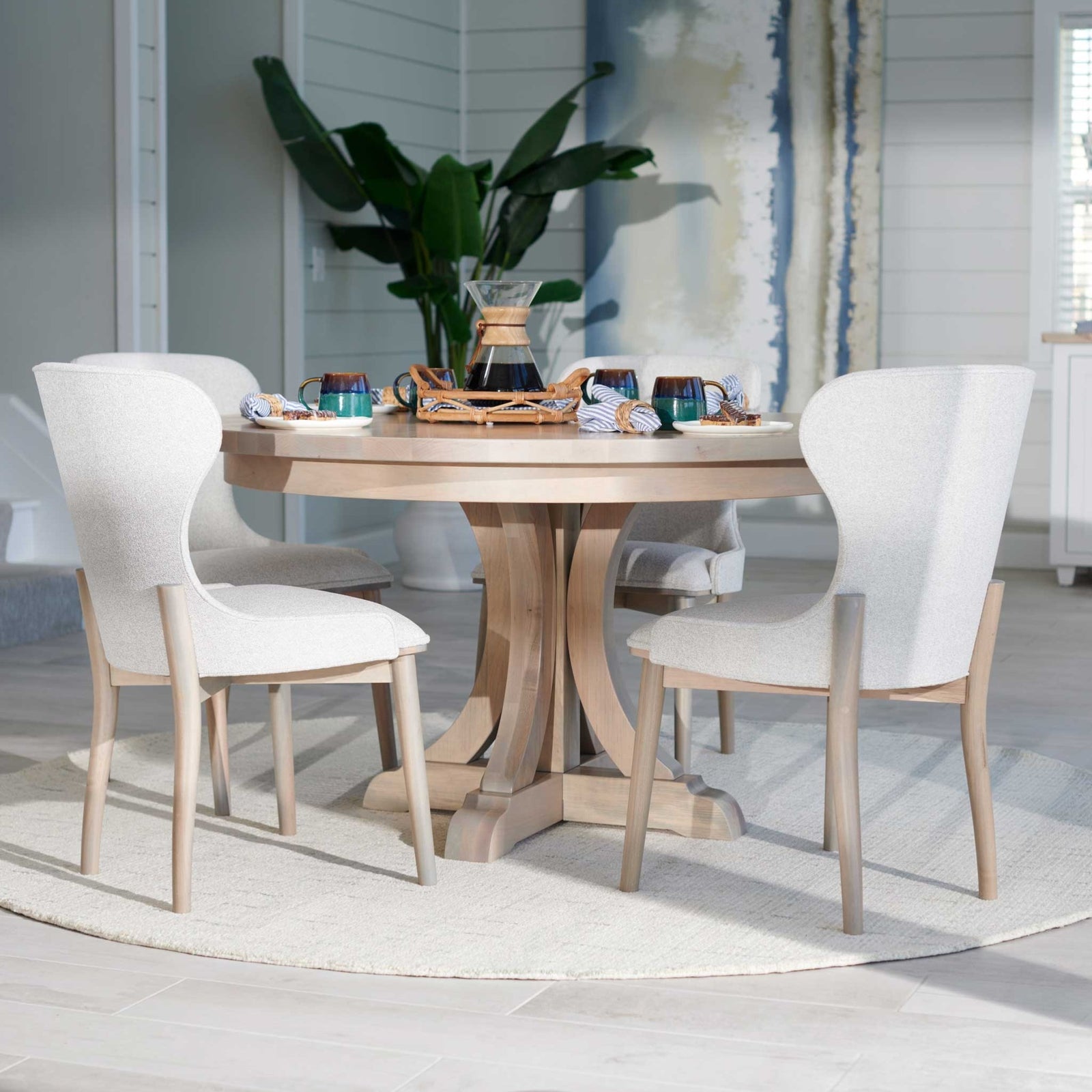 Whitewashed round pedestal table set with a pour-over coffee carafe, mugs and two ivory curved-back chairs