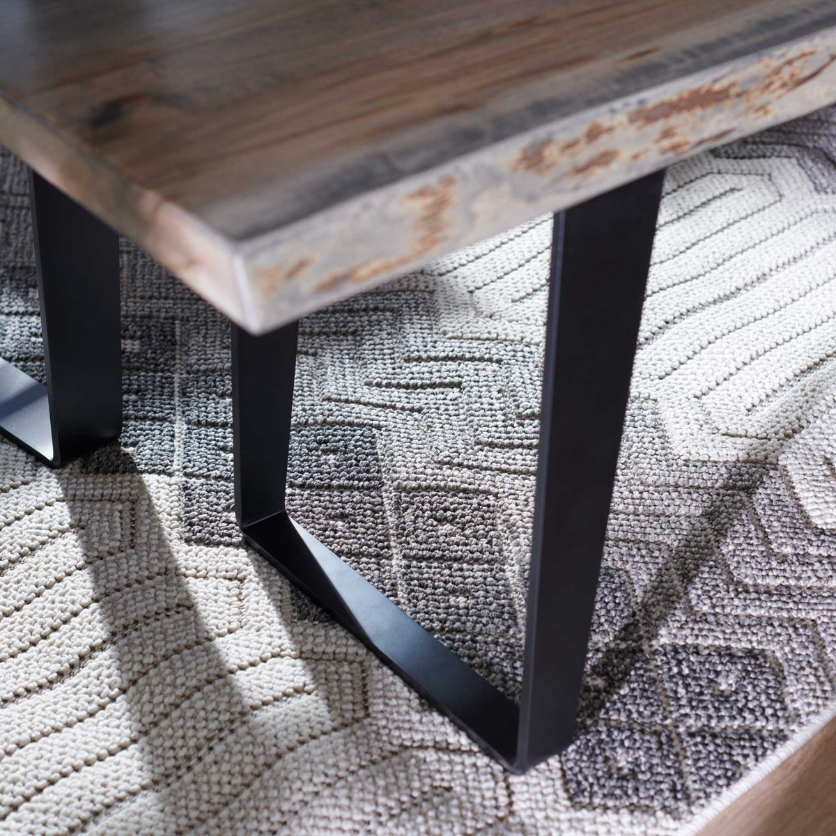 Close-up of a live edge bench slab with bark-line inclusions on black angled steel legs over a gray patterned rug