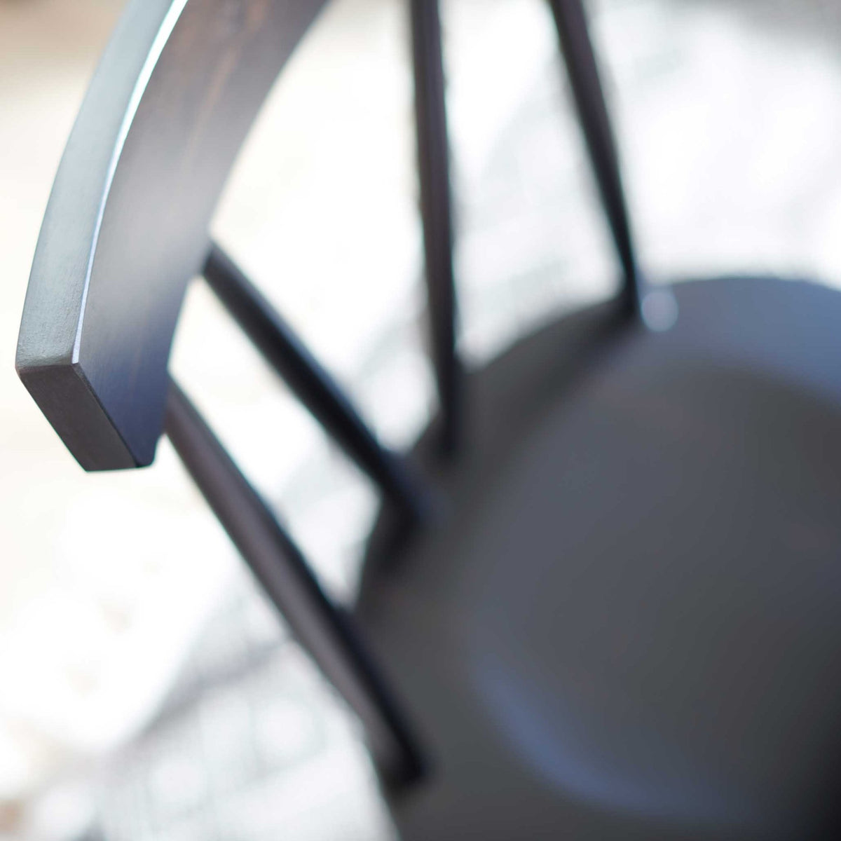 Close-up of a black Windsor chair's curved crest rail and slim spindles above its dark seat