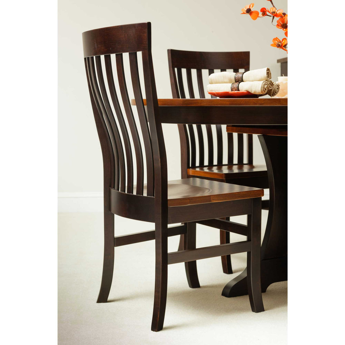 Two-tone dining chairs with black frames and cherry seats pulled up to a round pedestal table in a neutral dining room