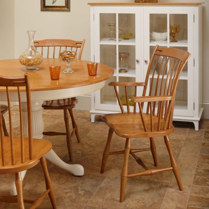 Cherry thumb back Windsor arm chair beside a two-tone pedestal table and white glass door display cabinet