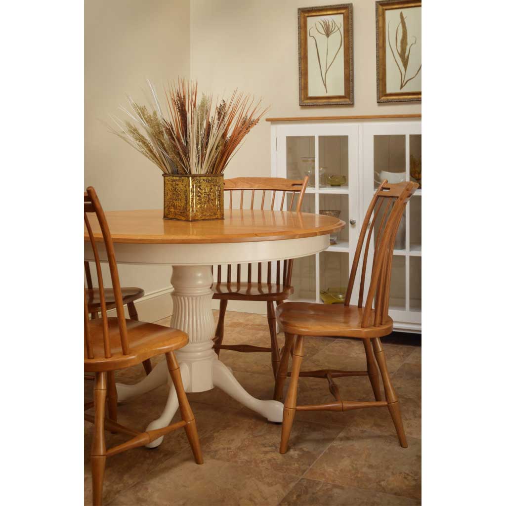 Two-tone round pedestal table in cherry with a white base surrounded by thumb back spindle chairs and dried wheat