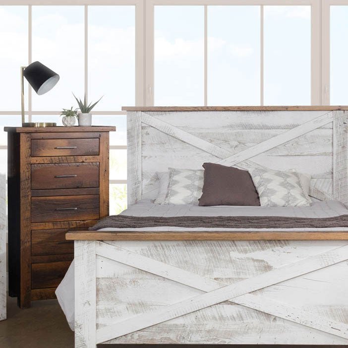 Bedroom corner showing a distressed white X-panel bed beside a five-drawer brown reclaimed wood lingerie chest