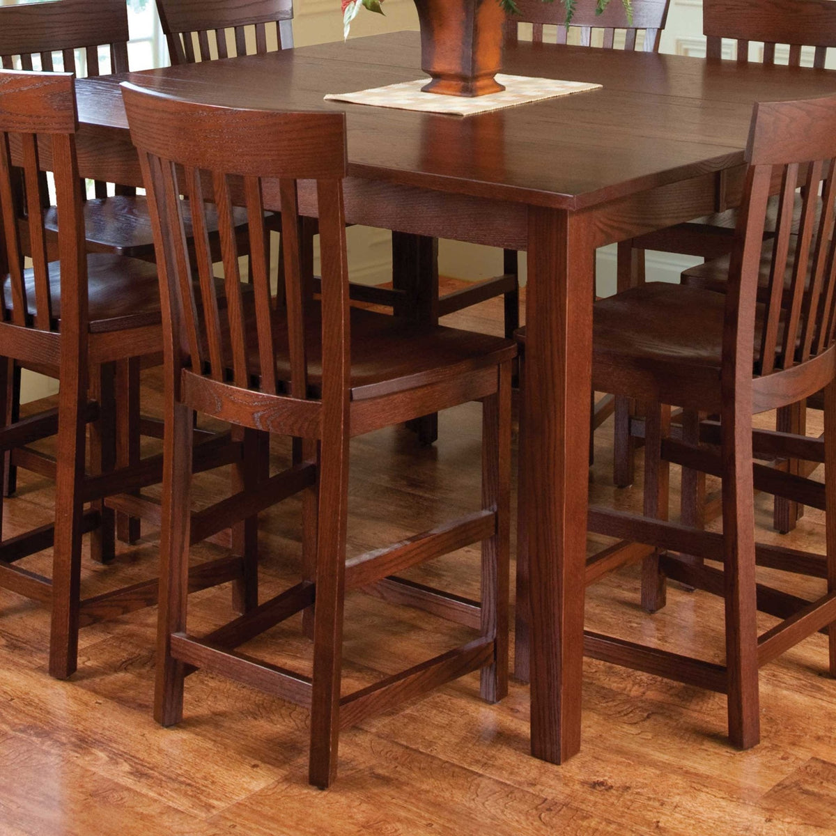 Dark oak counter height stools with slat backs tucked under a matching square pub table on wood flooring