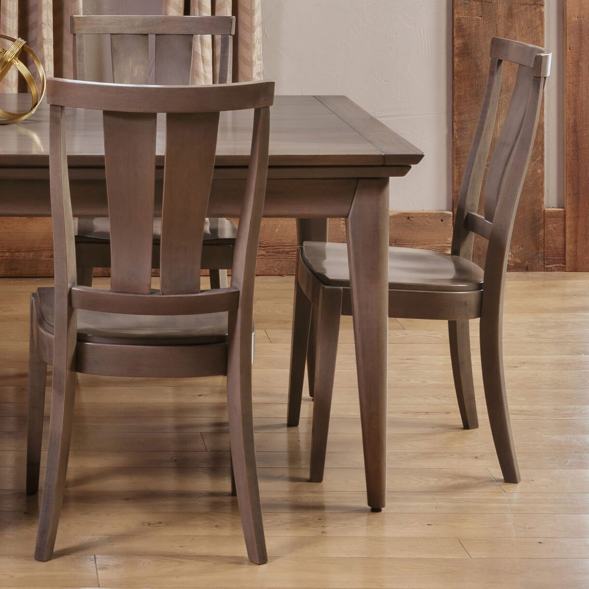 Two gray brown modern dining chairs with curved splat backs and saddle seats at a plank top dining table