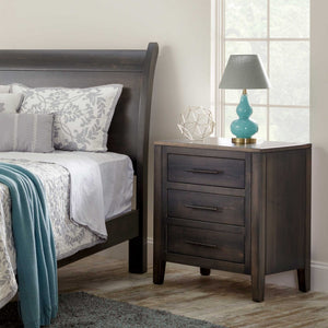 Weathered gray three drawer nightstand with black bar pulls beside a matching sleigh bed and teal lamp in a sunny bedroom
