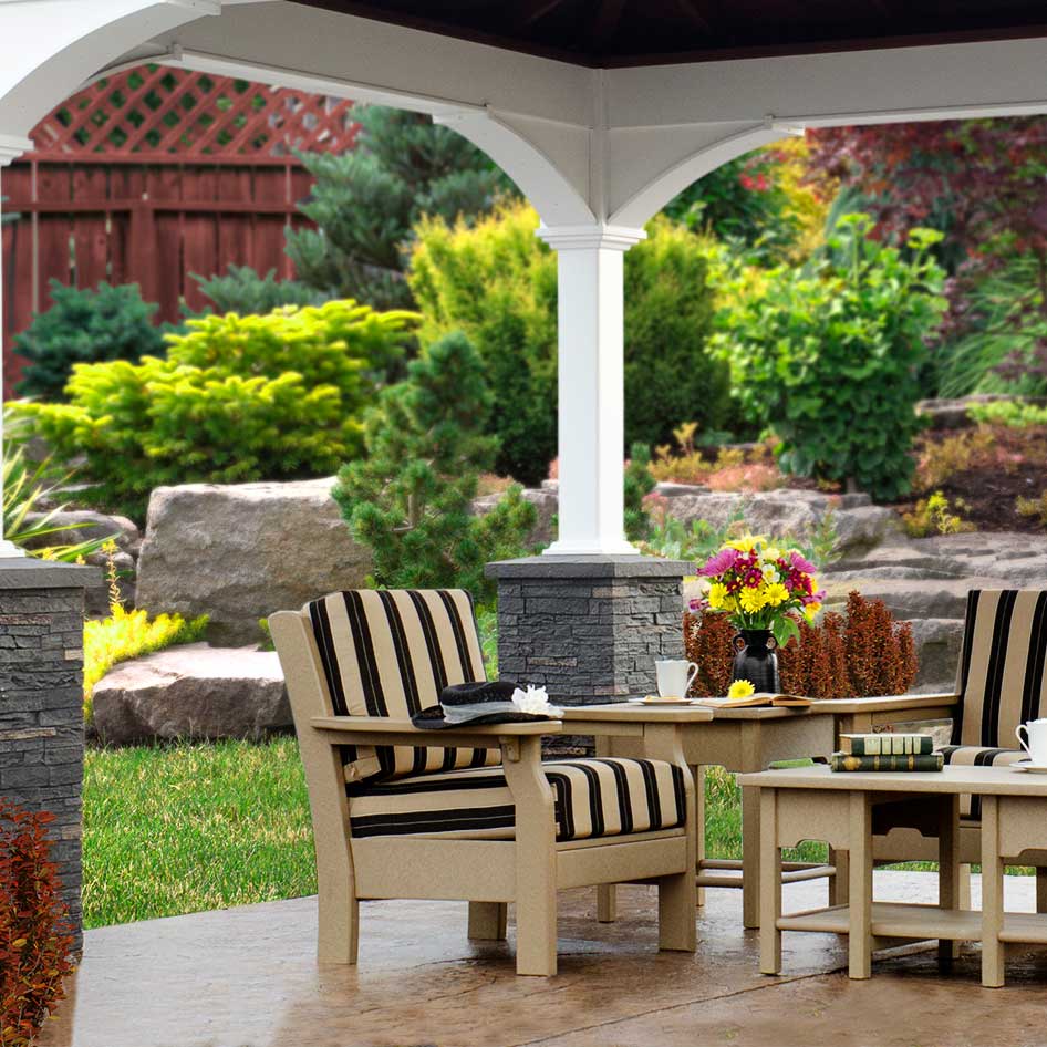 Tan poly patio chairs with black and cream striped cushions under a white pavilion beside a landscaped garden