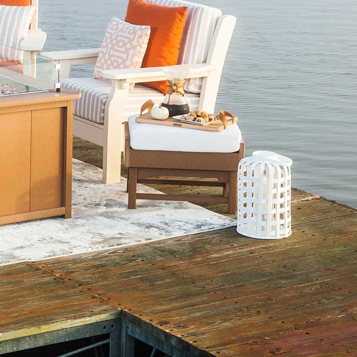 White poly patio chair and cushioned ottoman with a serving tray of snacks on a dock beside a cedar fire table