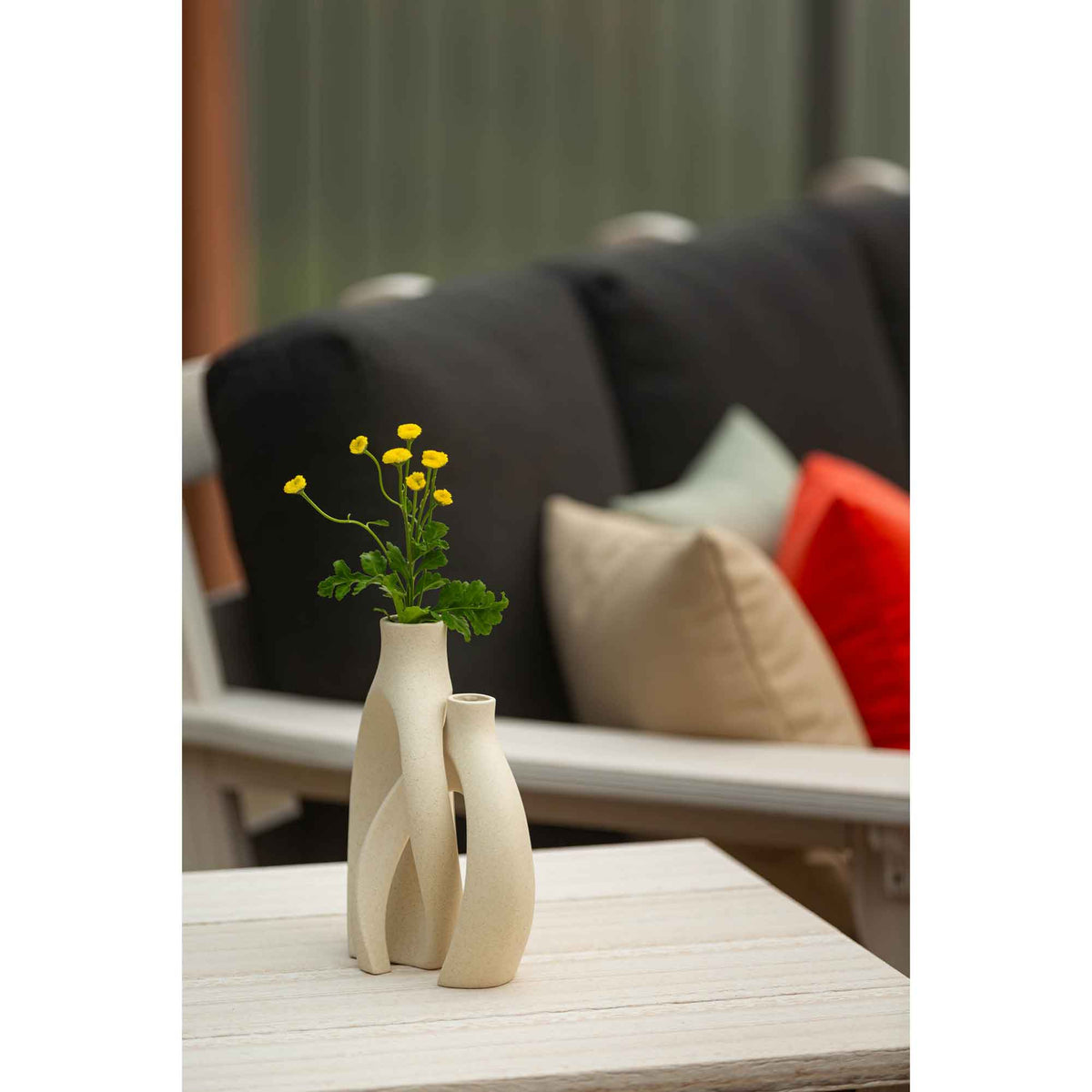 Cream ceramic bud vases with yellow flowers on a white poly table in front of a black cushioned patio sofa
