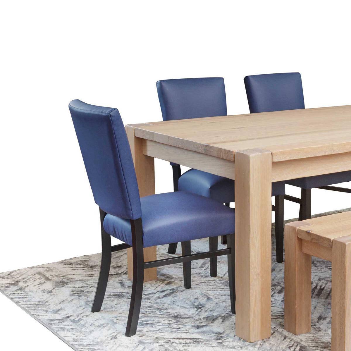 Navy blue leather dining chairs with black legs at a pale white oak dining table and bench on a gray patterned rug