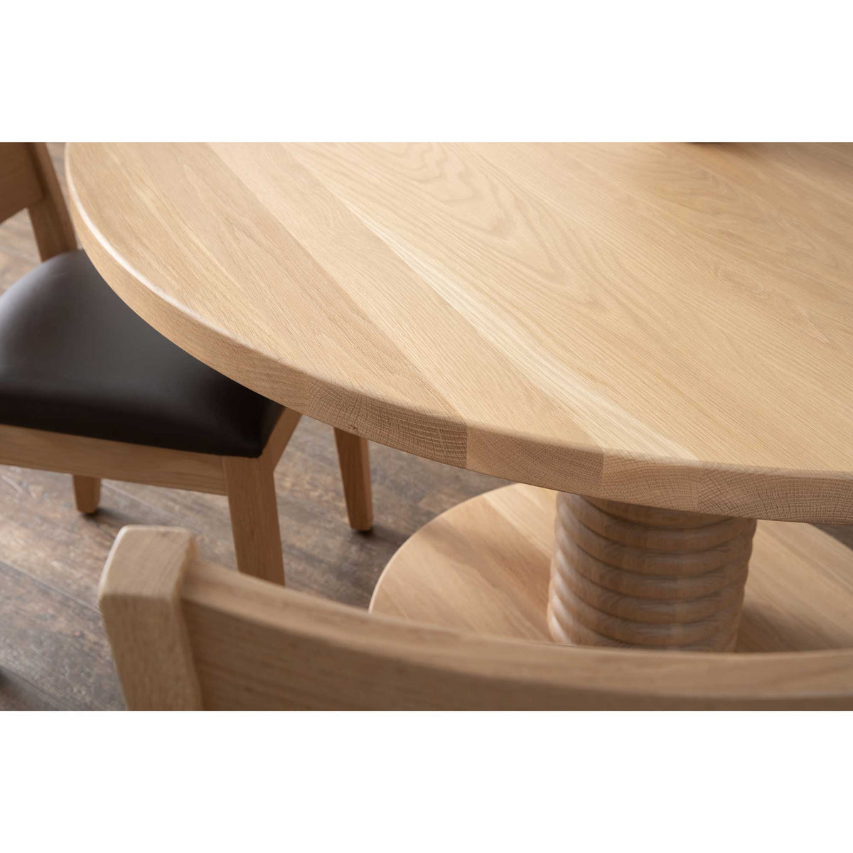 Close-up of the round oak tabletop edge and ribbed pedestal column with a leather seated chair alongside