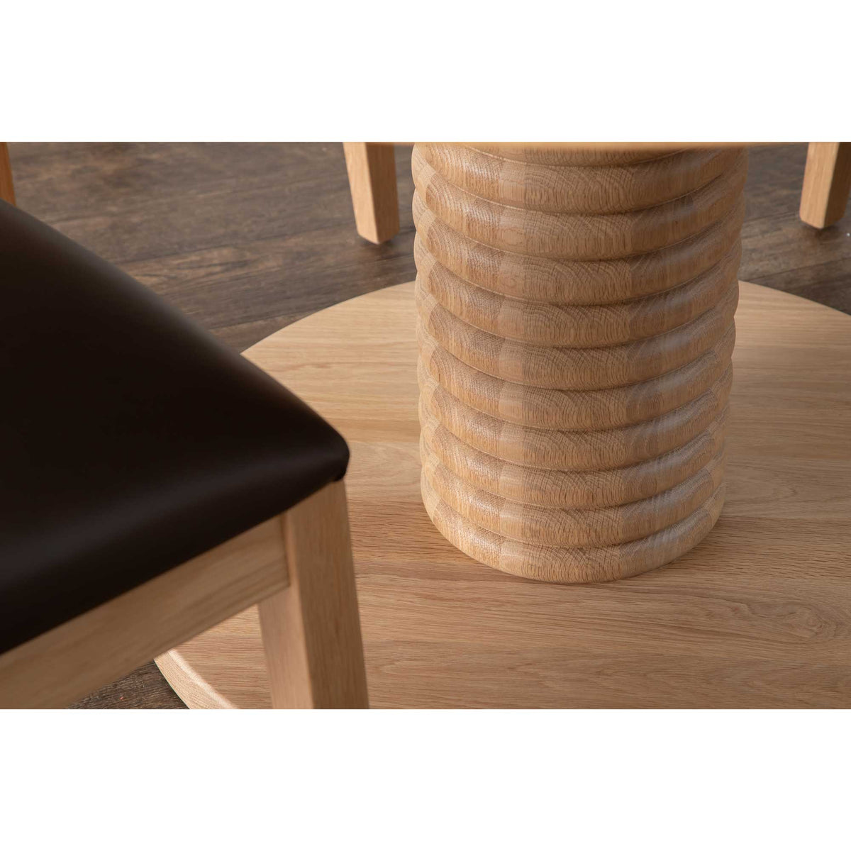 Detail of the sculpted ring pedestal column and round base of a white oak dining table on dark plank flooring