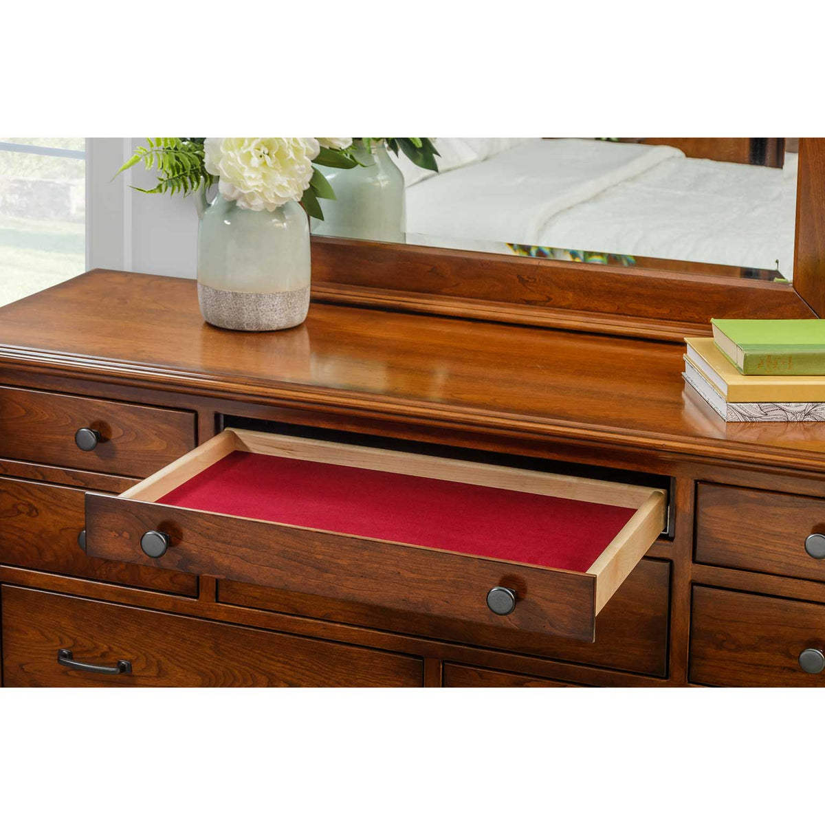 Open felt lined jewelry drawer in red on a cherry dresser with dark round knobs and mirror above