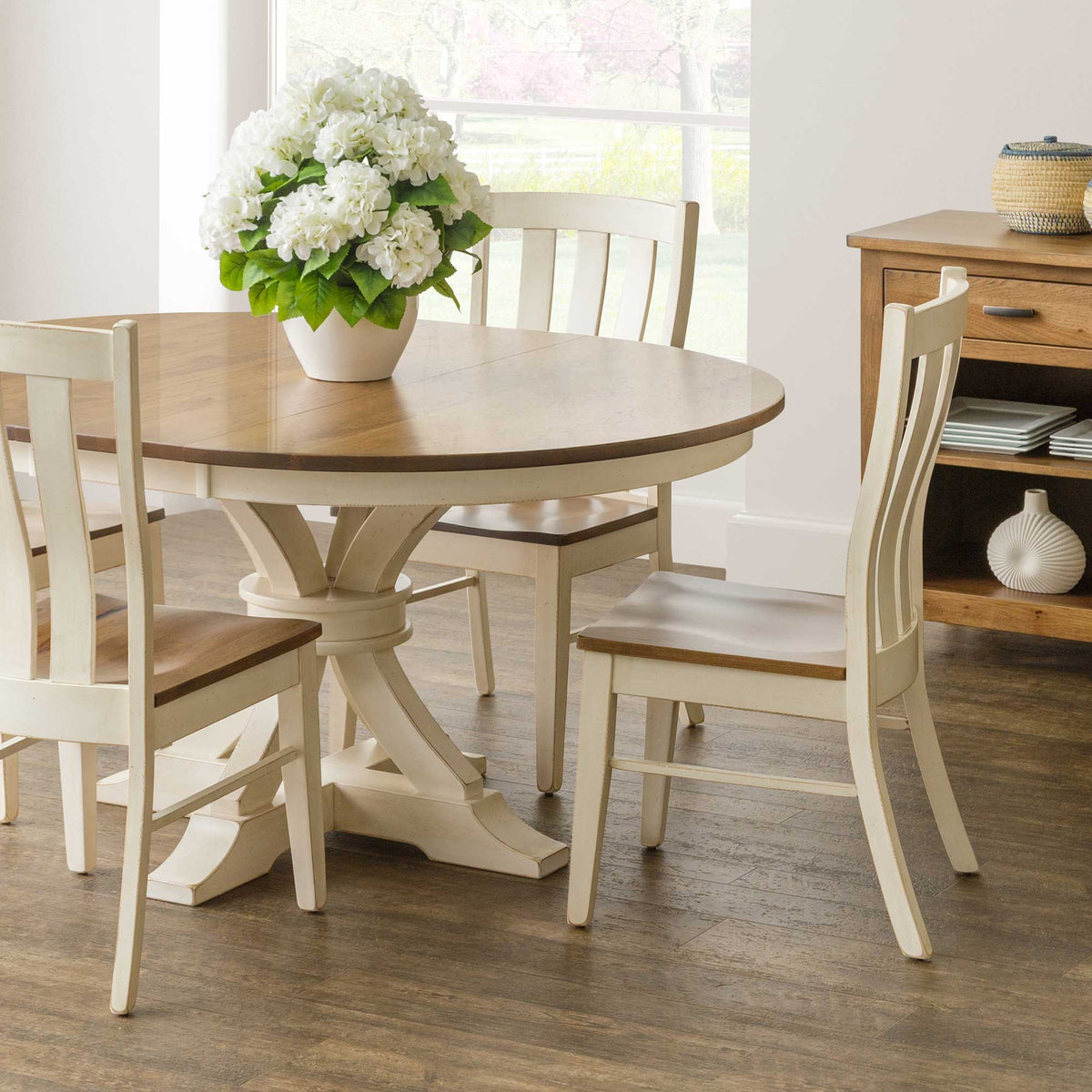 Cream painted Willow lumbar dining chairs with curved slat backs and natural wood seats around a round two-tone pedestal table
