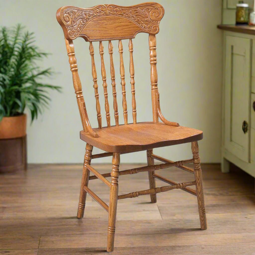 Oak pressback side chair with a carved floral crest and turned spindles beside a green cupboard and fern