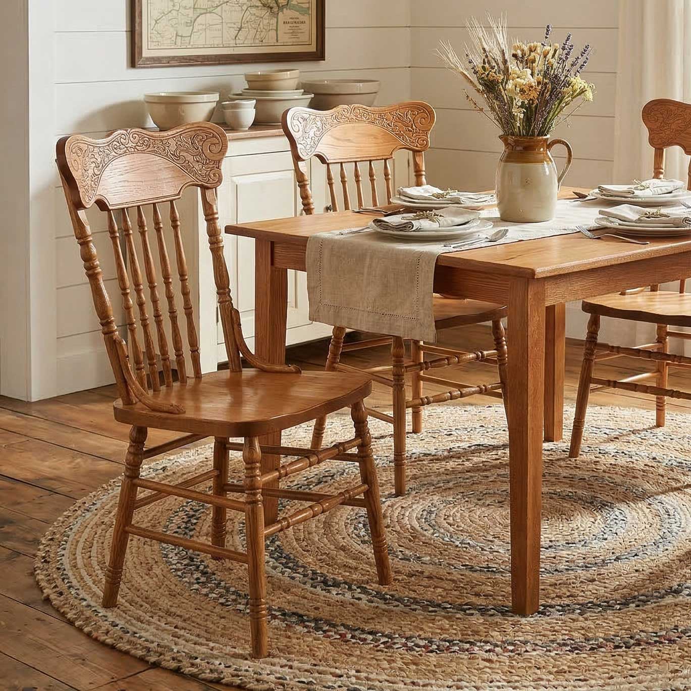 Oak pressback chairs with ornate scrolled crest carving and turned spindles at a farm table on a braided rug