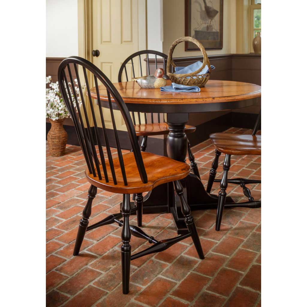 Round two-tone dining table with black bow back Windsor chairs and cherry seats on a red brick floor